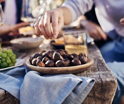 A person is taking roasted chestnuts out of a wooden bowl