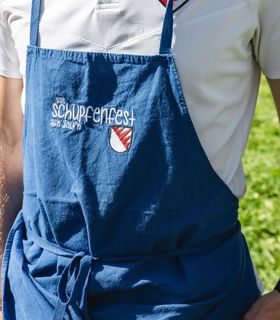 Ein Mann in traditioneller Kleidung hält ein Glas Weißwein und ein Stück Fingerfood in den Händen