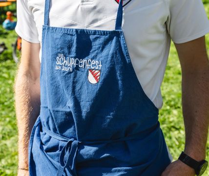 Ein Mann in traditioneller Kleidung hält ein Glas Weißwein und ein Stück Fingerfood in den Händen