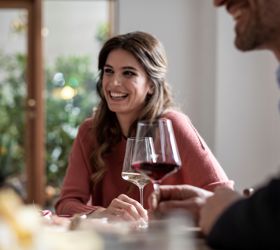 Lachende Frau beim Gespräch mit einem Mann bei einem Glas Wein in gemütlicher Atmosphäre.