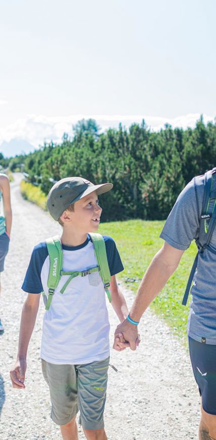 Smiling family hiking on a sunny trail with wooden fence and green landscape.