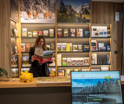 Eine Frau liest eine Broschüre vor einem Regal mit Infomaterial im Tourismusbüro
