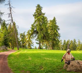 Forest path with wooden fence and a statue made of fabric and metal on a rock beside the trail.