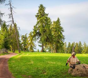 Forest path with wooden fence and a statue made of fabric and metal on a rock beside the trail.