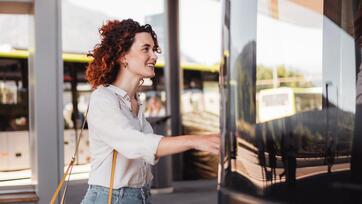Frau steigt an einer modernen Bushaltestelle lächelnd in einen grünen Bus ein.