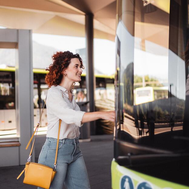 Woman smiling as she boards a green bus at a modern bus stop.