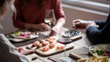 Drei Personen genießen eine Südtiroler Marende mit Wein, Käse, Speck und Aufschnitt.