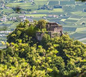 Castle ruins on wooded hill, surrounded by green fields and villages in the valley.