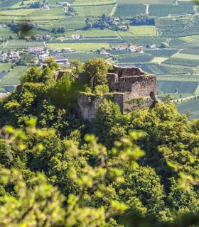 Castle ruins on wooded hill, surrounded by green fields and villages in the valley.