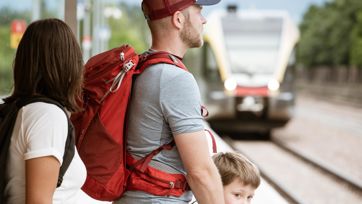 Family with backpacks waiting on the platform for an approaching train.