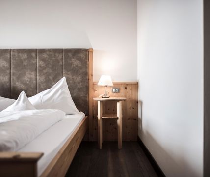 Cozy bedroom with wooden bed frame, padded headboard, white bedding, and a bedside table with a lamp.